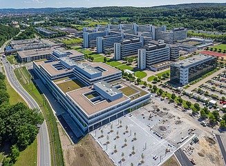 Universitätscampus von oben mit drei flachen Blocks und Parkplatz im Vordergrund und 5 riegelförmigen Bauten dahinter