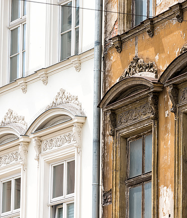 Historisches Gebäude mit einer alten Fassade in braun und einer neuen sanierten Fassade in strahlenden weiß