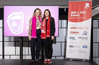Zwei Personen stehen auf einer Bühne vor einem pinken Bildschirm mit dem Text „Die Stadt liest Bestand“ und einem großen Mund-Logo; daneben ein rotes Event-Banner mit Sponsorenlogos.
