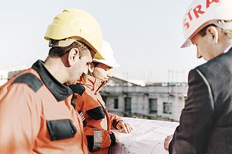 STRABAG Baustellenmitarbeiter Zu sehen sind mehrere STRABAG Baustellenmitarbeiter die sich über Sanierung und Umbau einer Bestandsimmobilie unterhalten