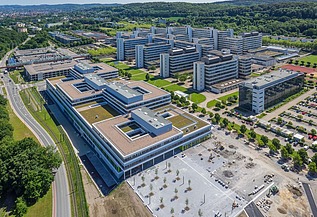 Universitätscampus von oben mit drei flachen Blocks und Parkplatz im Vordergrund und 5 riegelförmigen Bauten dahinter