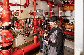 Mitarbeiter steht vor Sprinkleranlage mit Tablet in der Hand
