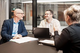 Drei Mitarbeiter am Tisch mit Laptop und Papierunterlagen