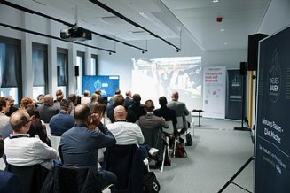 Fachforum mit Zuhörern die auf eine Leinwand schauen mit einem Banner zum Thema Bauen im Bestand