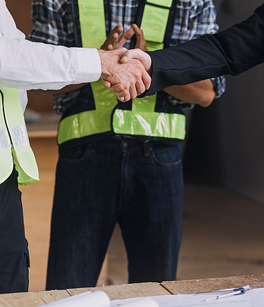 Handschlag zwischen zwei Personen mit Bauhelmen im Bauwesen